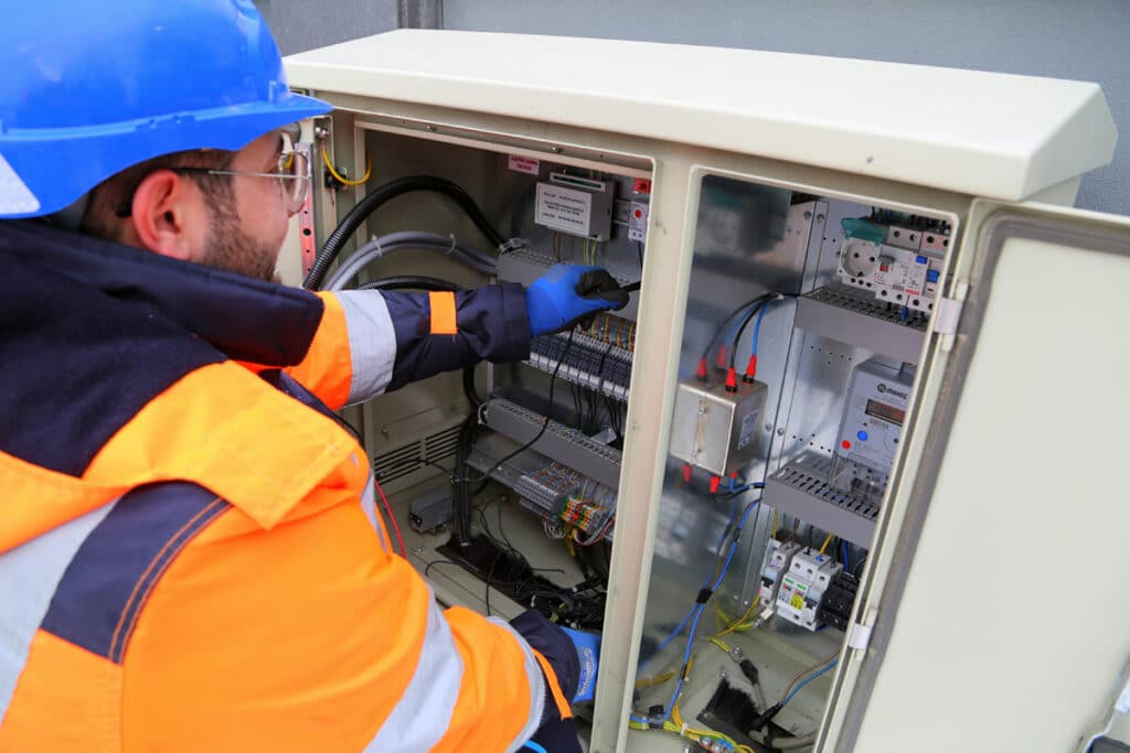 Certified electrician inspecting and working on wiring inside an electrical control cabinet.